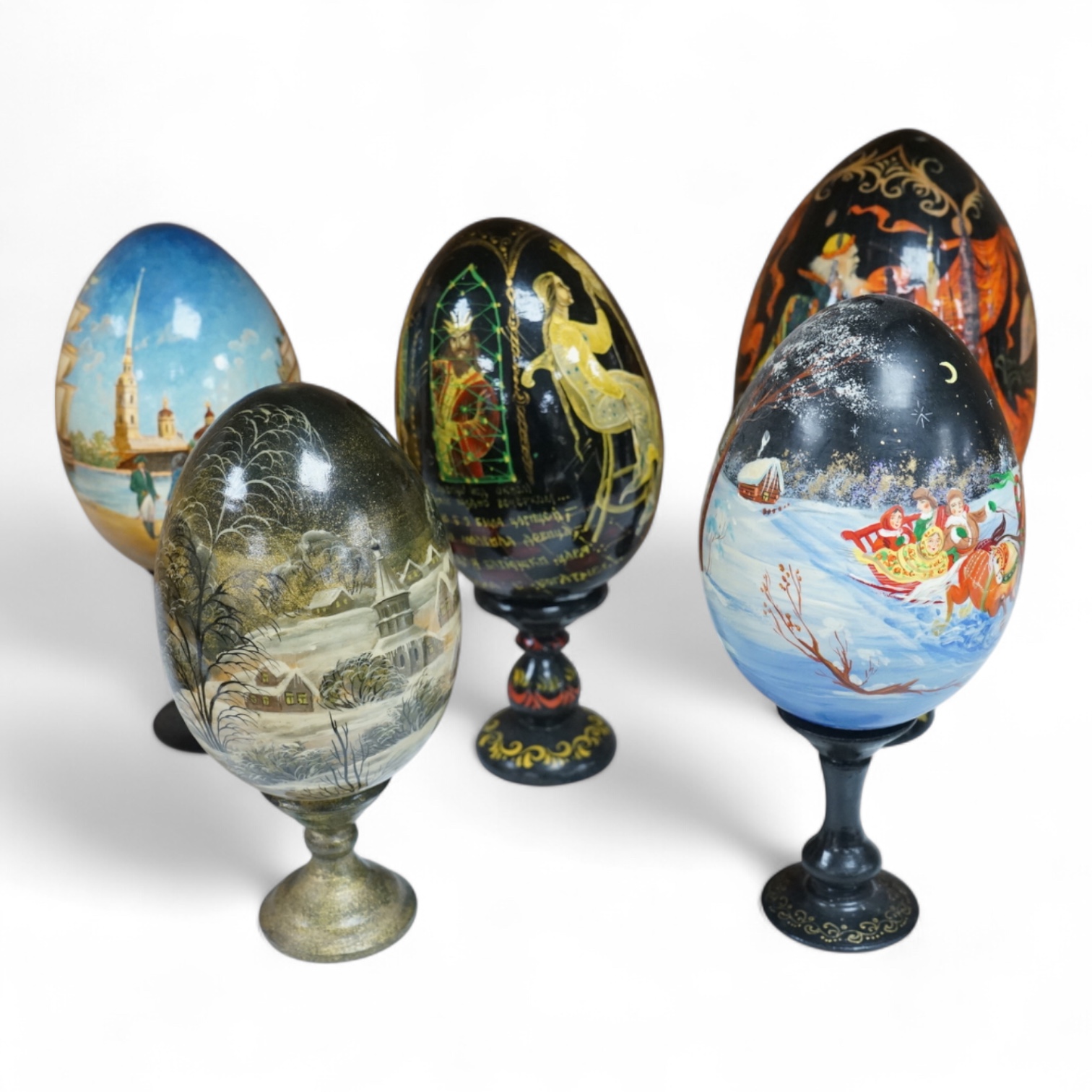 Five Russian painted and lacquered 'eggs' on stands, one inscribed in cyrillic, largest 21cm high
